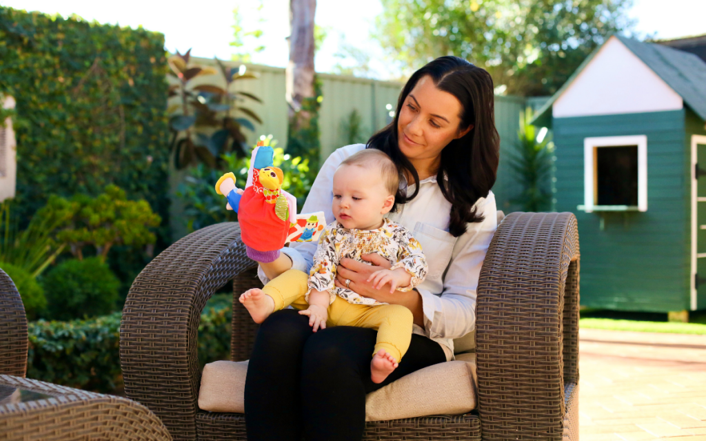 Mother sitting in a backyard with her baby holding a baby toy